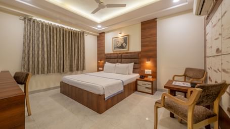 A well furnished spacious room with a king size bed, wooden furniture, and elegant curtains at Hotel Highway King, Jaipur.