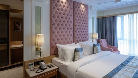 A room with a large bed featuring a pink tufted headboard, bedside tables, and an armchair with soft lighting - Melior Inn