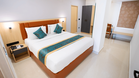 A spacious room with a large bed, a bedside table, and a doorway to the side at Sunrise Business Hotel, Hyderabad.