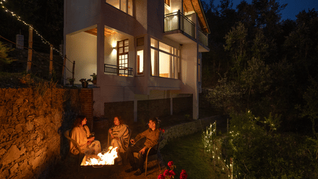 A group of people are sitting around a bonfire in front of a multi-story building at Ziran Retreat.
