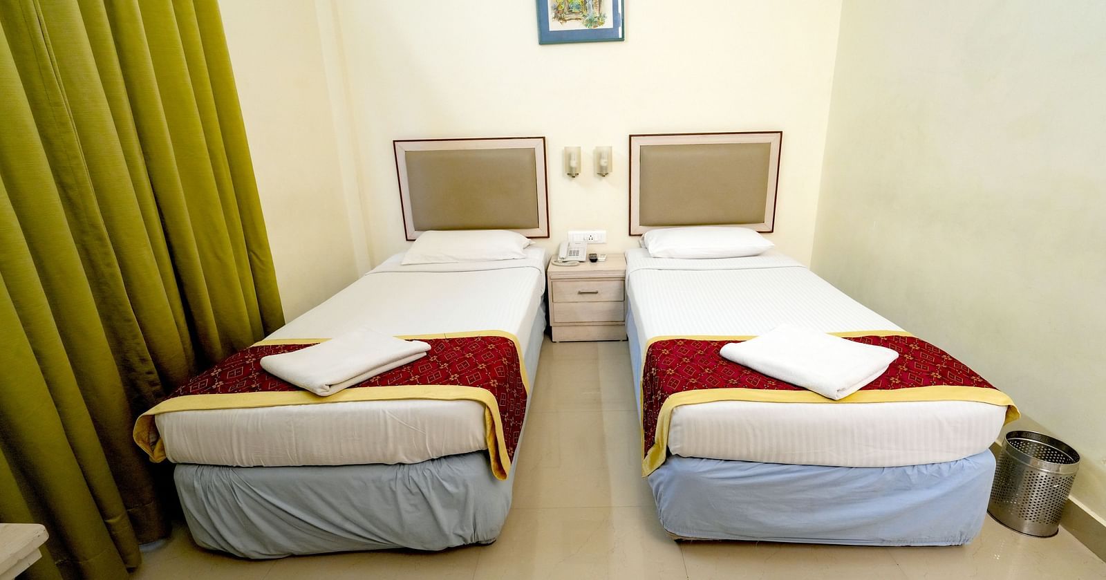A hotel twin bedroom with white and mustard bedding, green curtains, and a picture on the wall at Greens Inn - Comfortable Twin Rooms in Ramoji Film City.