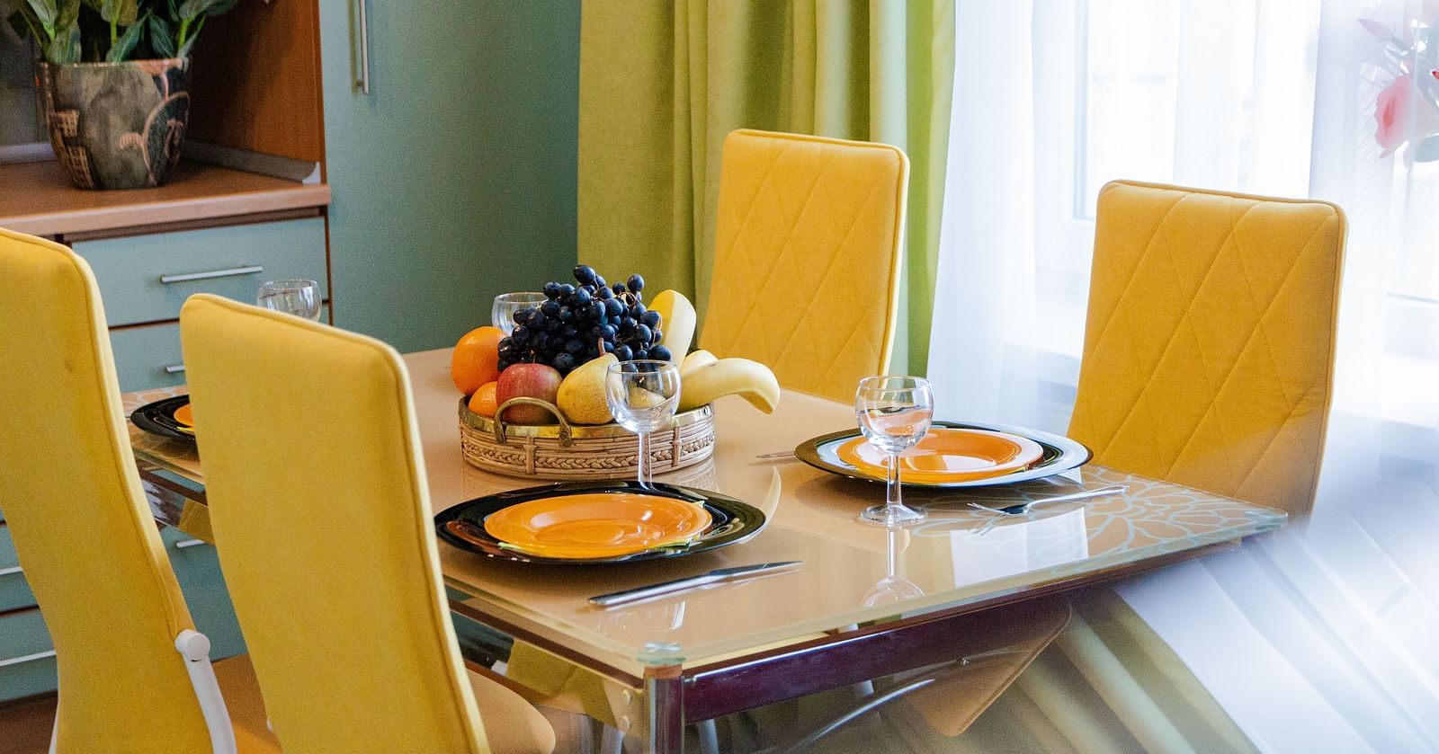 A dining table wth bright yellow chairs, set for a meal with plates and cutlery at  Sitara Luxury Hotel in Hyderabad near Ramoji Film City.