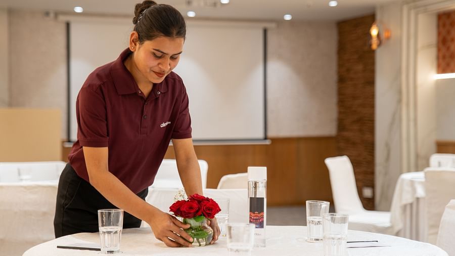 A hotel staff member is arranging a floral centerpiece on a round table in a conference room - Clarks Inn, Indore.