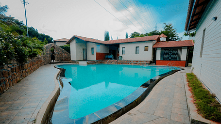 A uniquely shaped swimming pool at Nirantara Resort & Spa, Bengaluru, surrounded by plants and buildings.