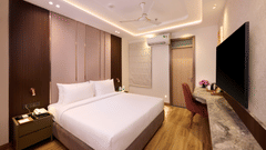 A bedroom in Tulip Inn Gurugram showing a wall-mounted flat-screen television across from a double bed with a high, padded headboard.