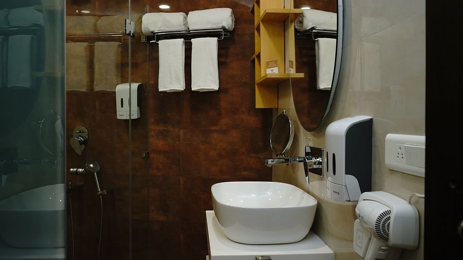 An image of a bathroom at Five Elements Hotels North Avenue, Delhi featuring sink and faucet, towel, handwash dispenser, shower glass, and other amenities