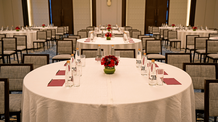 A banquet hall setup at The Residency Signature Madurai featuring round tables with tablecloths, chairs, notebooks, and centrepieces.