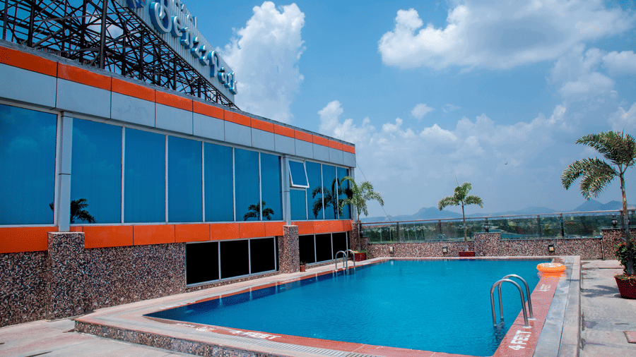 The rooftop swimming pool featuring a vast blue sky with clouds above the pool at the Benzz Park, Vellore.