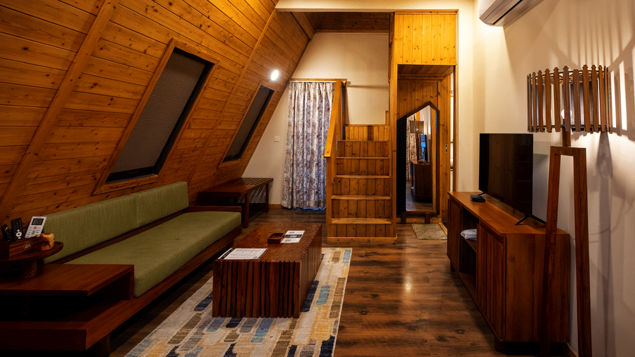 Sitting area with sofa and wooden walls inside a duplex villa at Hotel Sonar Bangla, Taki.
