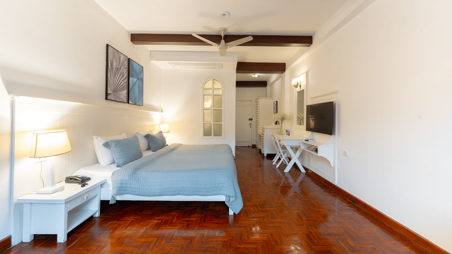 A long-angle shot of a modern guest room featuring white walls, a workspace, and a comfortable bed - Johnson Lodge & Spa, Manali