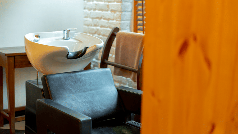 A modern salon-style hair wash station with a black leather chair and white ceramic basin - Johnson Lodge & Spa, Manali