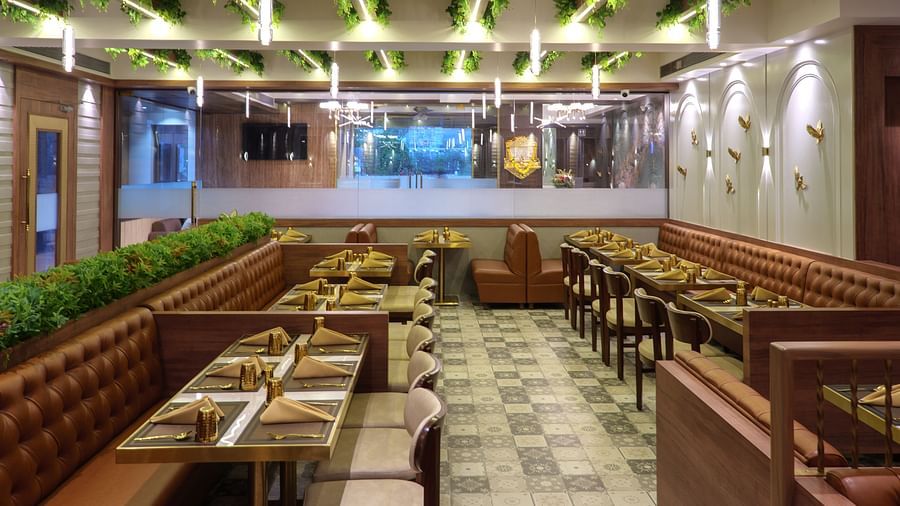 A spacious restaurant with numerous wooden tables and chairs, featuring bright overhead lighting and some greenery - Melior Inn