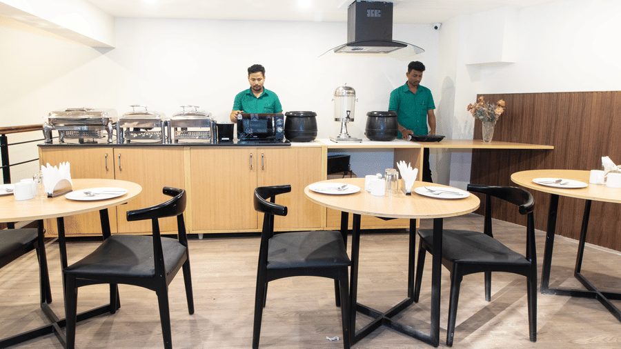 Sanctum Suites, Richmond Road, Bangalore includes a dining space with wooden tables, black chairs, a buffet counter with food warmers, and staff in uniforms.