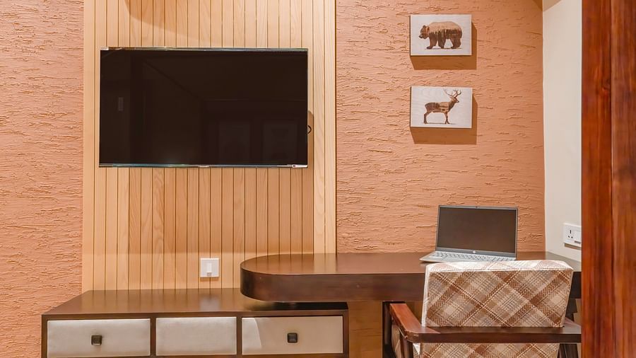 View of the desk, television right above it, and a table with a chair beside it, along with small wall-mounted frames at The Chamomile Estate.