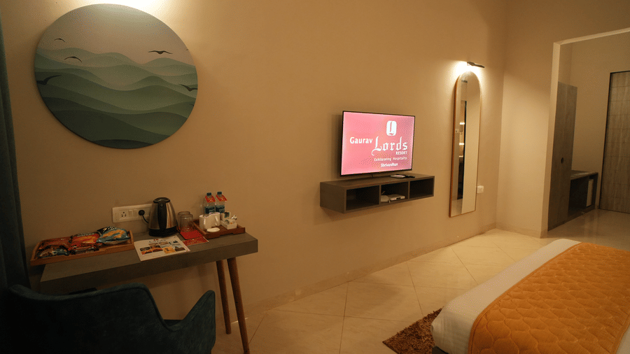 A dimly lit room with bed, TV, mirror and table with coffee station on it