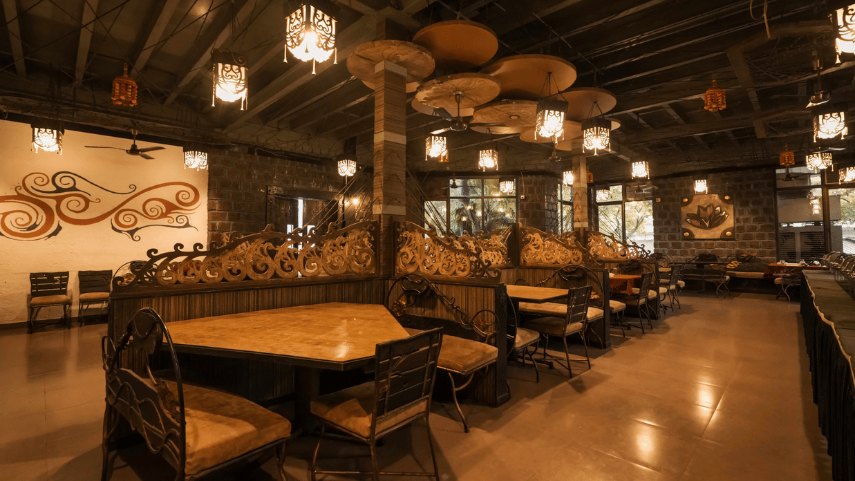 Interior view of a dark, ambient dining hall featuring high-backed booths and elaborate ceiling decorations at Adamo The Village.