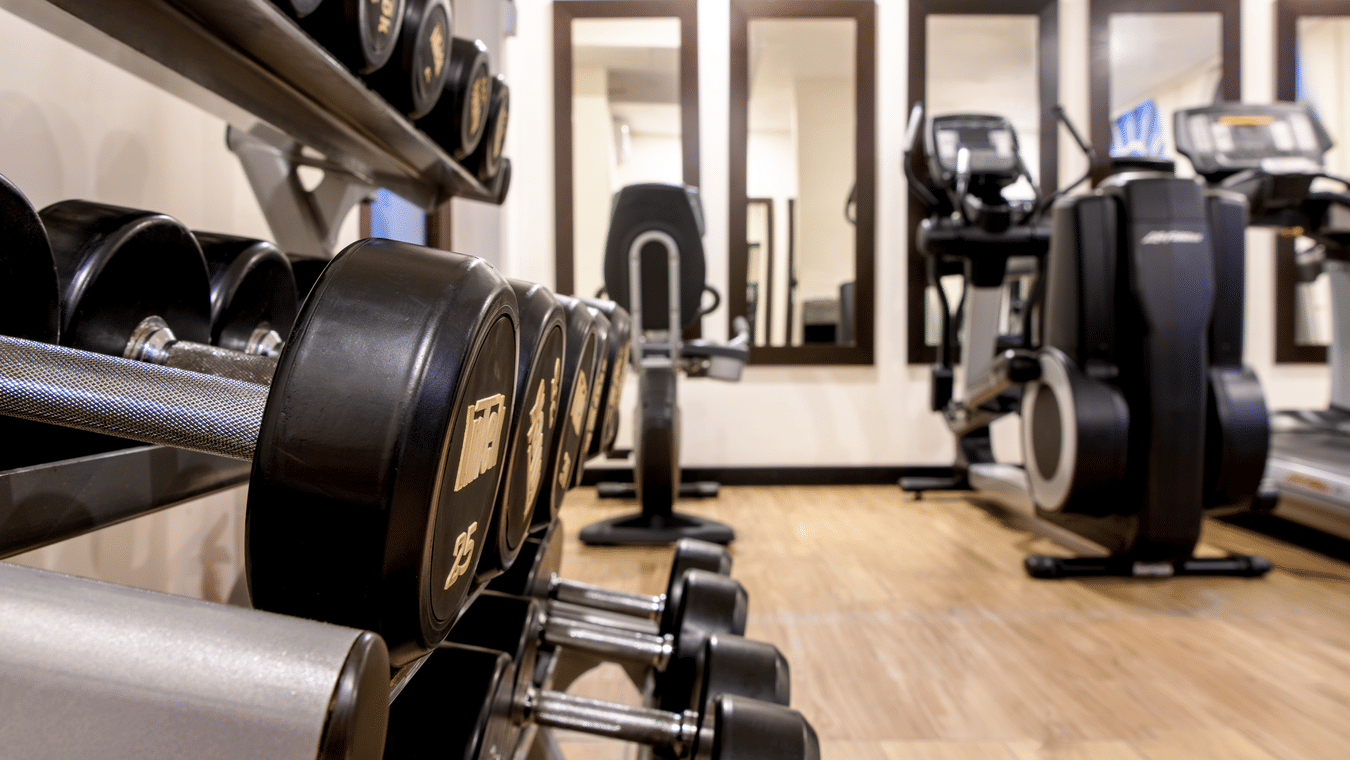 A close-up of a dumbbell rack with cardio machines visible in the background inside the fitness center at S Hotel Kingston.
