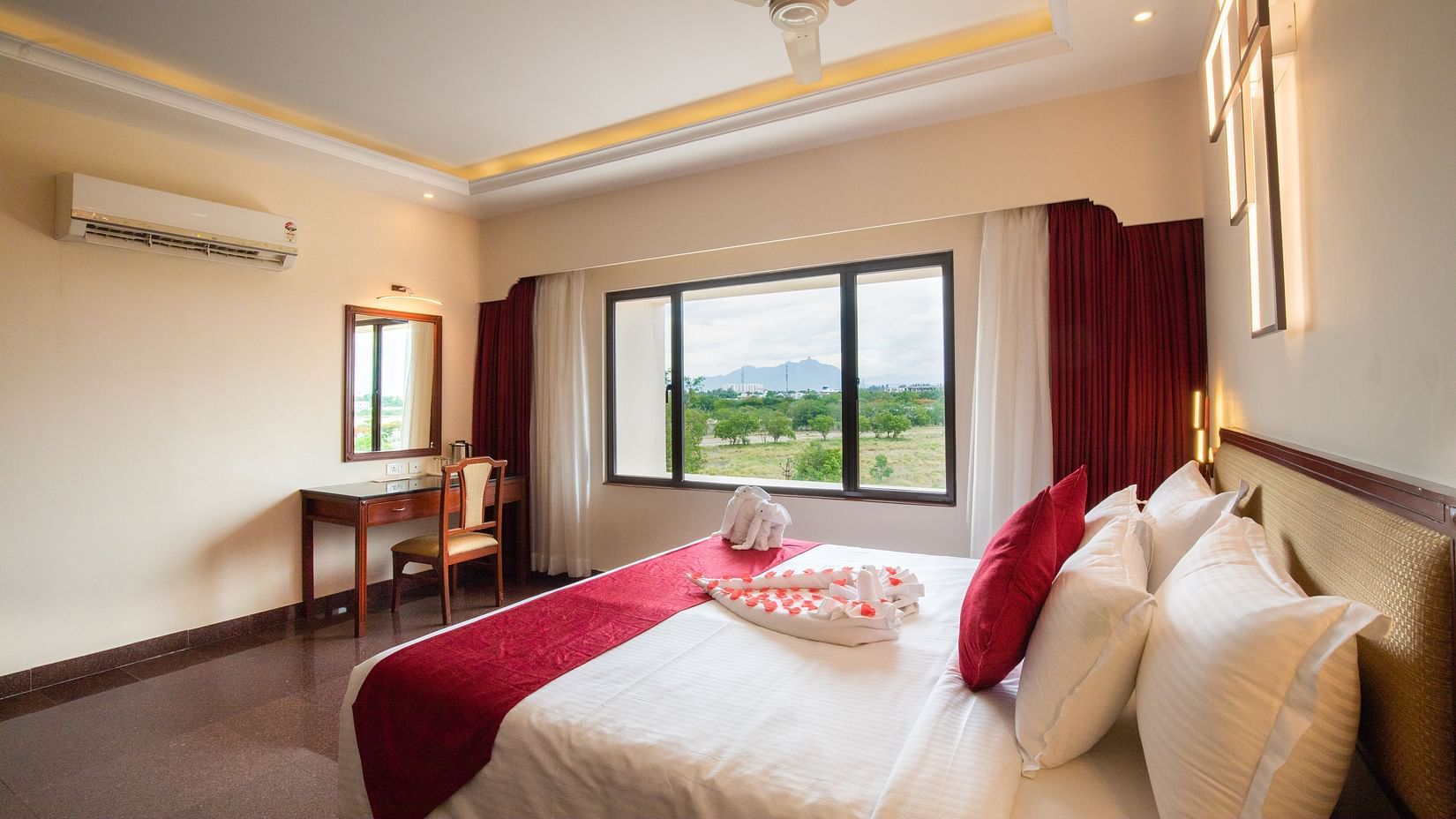 A bright, modern Presidential Suite with a king sized bed, a desk and chair by the window, and a scenic view of greenery and mountains outside
