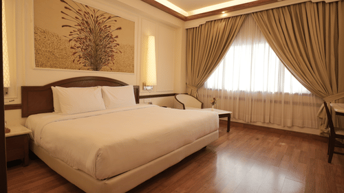 A well-lit bedroom with a king size bed, wooden flooring, curtains, and a seating area, reflecting comfortable rooms in Jaipur - Clarks Amer, Jaipur