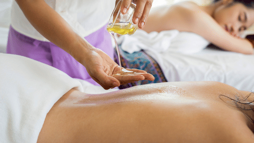 a person receiving back massage and oil being poured by a masseur