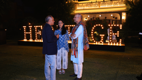 Two guests having a conversation in front of the glowing 'Heritage' signage during an evening event.