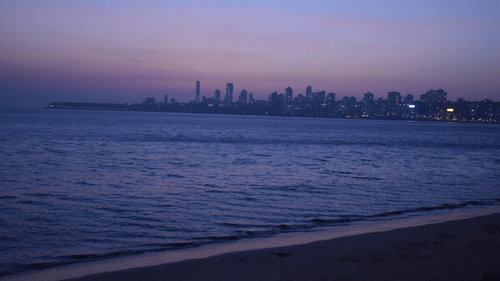 reflection of sky in shades of blue after sunset in the sea water by Juhu Beach with skyscrapers in the background