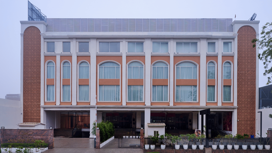 Skywings Sarovar Portico Mathura hotel exterior daytime view with arched windows, cream facade, manicured entrance garden, and overcast sky backdrop.