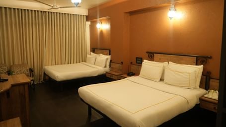 Bedroom with two double beds, curtains and warm lighting at Infiniti Hotel, Indore.