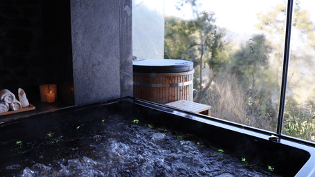 A bathing tub with water boiling next to a window which provides views of the outdoor.