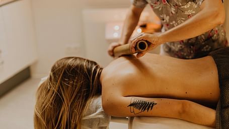 A therapist using a bamboo roller on a woman's shoulder.