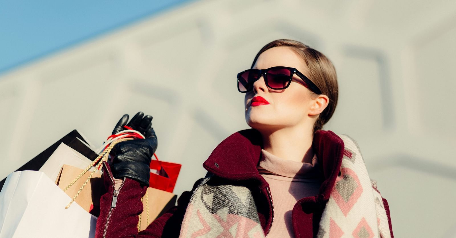 A close up shot of a woman basking in the sun holding many shopping bags.