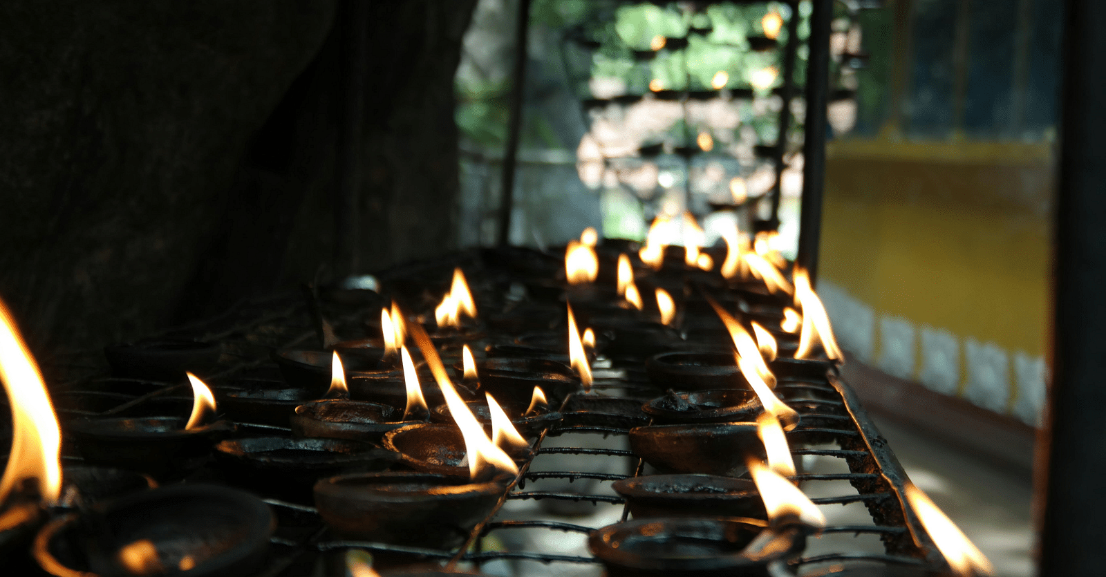 A close-up shows rows of lit oil lamps.