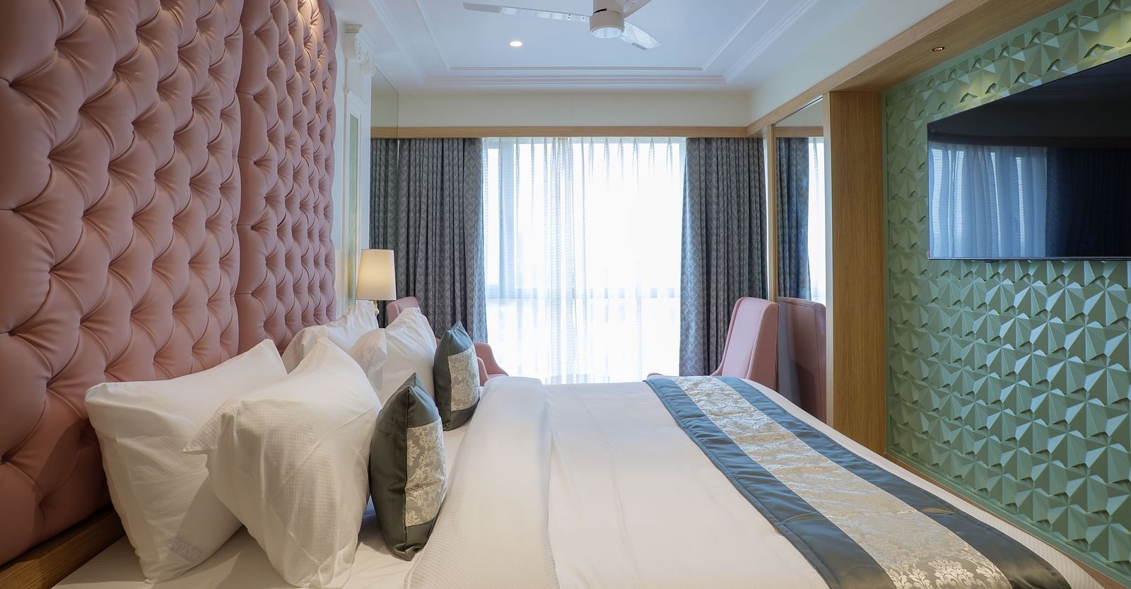 A modern hotel room features a bed with white linens and a television mounted on the wall - Melior Inn