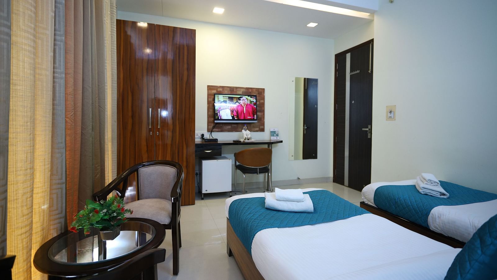A room with two single beds and a seating area, featuring warm lighting and a mirror on the wall - Asian Suites Cyber Park, Gurgaon