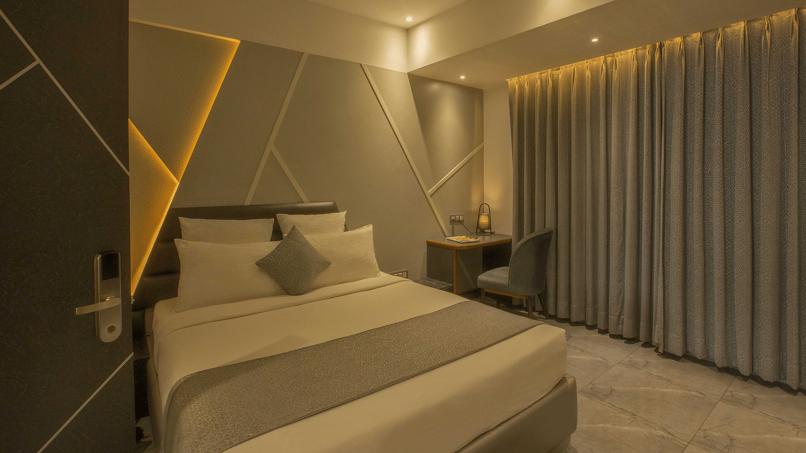 Image of well lit Coral Premium Room at Coral Reef Hotel and Spa in Port Blair featuring a plush bed and a work desk and chair next to it near the window