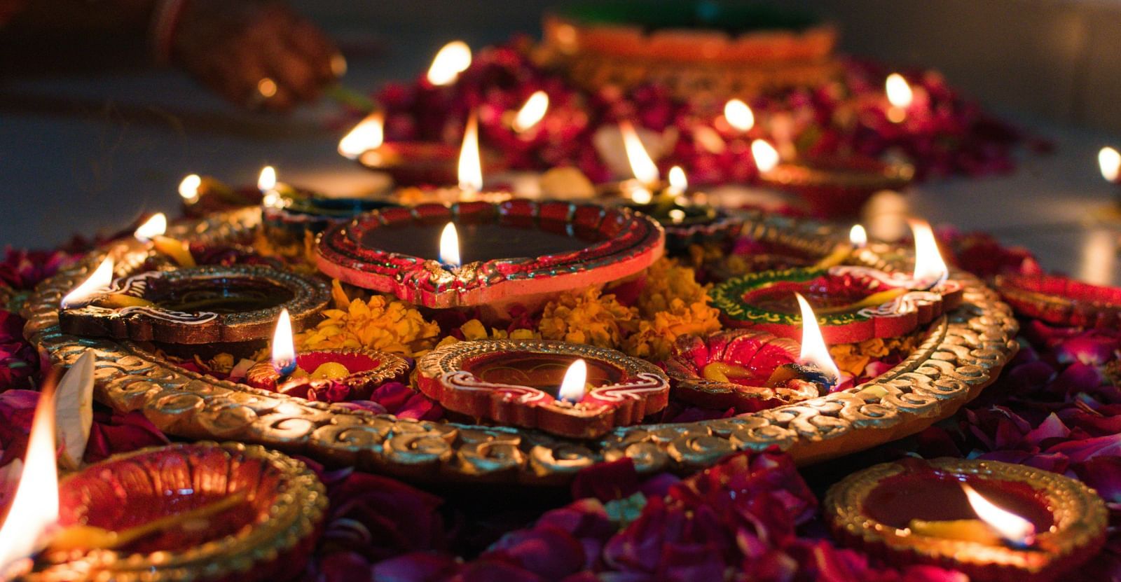 Small oil lamps lit during a hindu festival and the lamps are surrounded with flowers and loose petals.