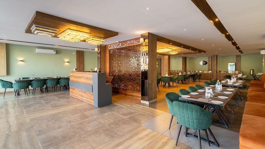 The restaurant image shot from a different angle of DLS Ganga Bliss, Haridwar with chairs, tables and warm lighting