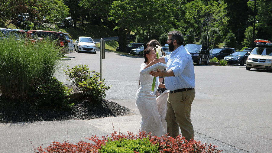 the bride going in for a hug with a person who is holding in a gift in one hand dressed in casual formals - Historic Tapoco Lodge