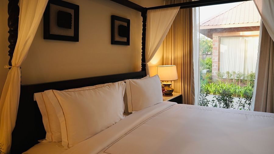 A bedroom with neatly arranged bed and photo frames on the wall and a view outside through the window.