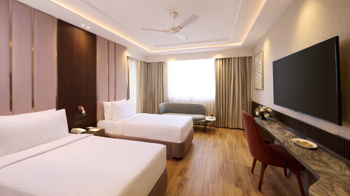 Twin bedroom at Tulip Inn Gurugram showing 2 separate beds, a long marble-topped work desk, a chair, and light-coloured curtains.