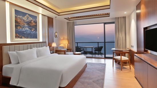 An Executive Room at Royal Tulip Shivapuri National Park - Kathmandu featuring a white king bed, mountain artwork, and a balcony with a sunset view.