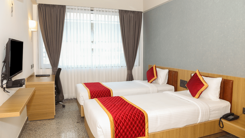Two single beds, a window with curtains, and a wooden desk at Icon Express By Bhagini, Mahadevapura.