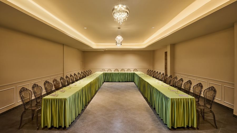 Elegant conference room with U-shaped table arrangement, transparent chairs, green table skirting, and ambient lighting from crystal chandeliers - Voyage The Solitaire Bliss.