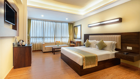 Deluxe Room at Summit North Star, Gangtok featuring a bed, a flat TV screen, a cabinet with tea and coffee maker, a mirror, work desk and chair, and a sofa set with centre table.