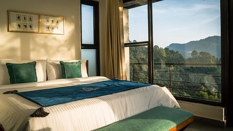 A bedroom with a balcony offering a mountain view and sunlight streaming in at BluSalzz Escapade Resort, Lansdowne