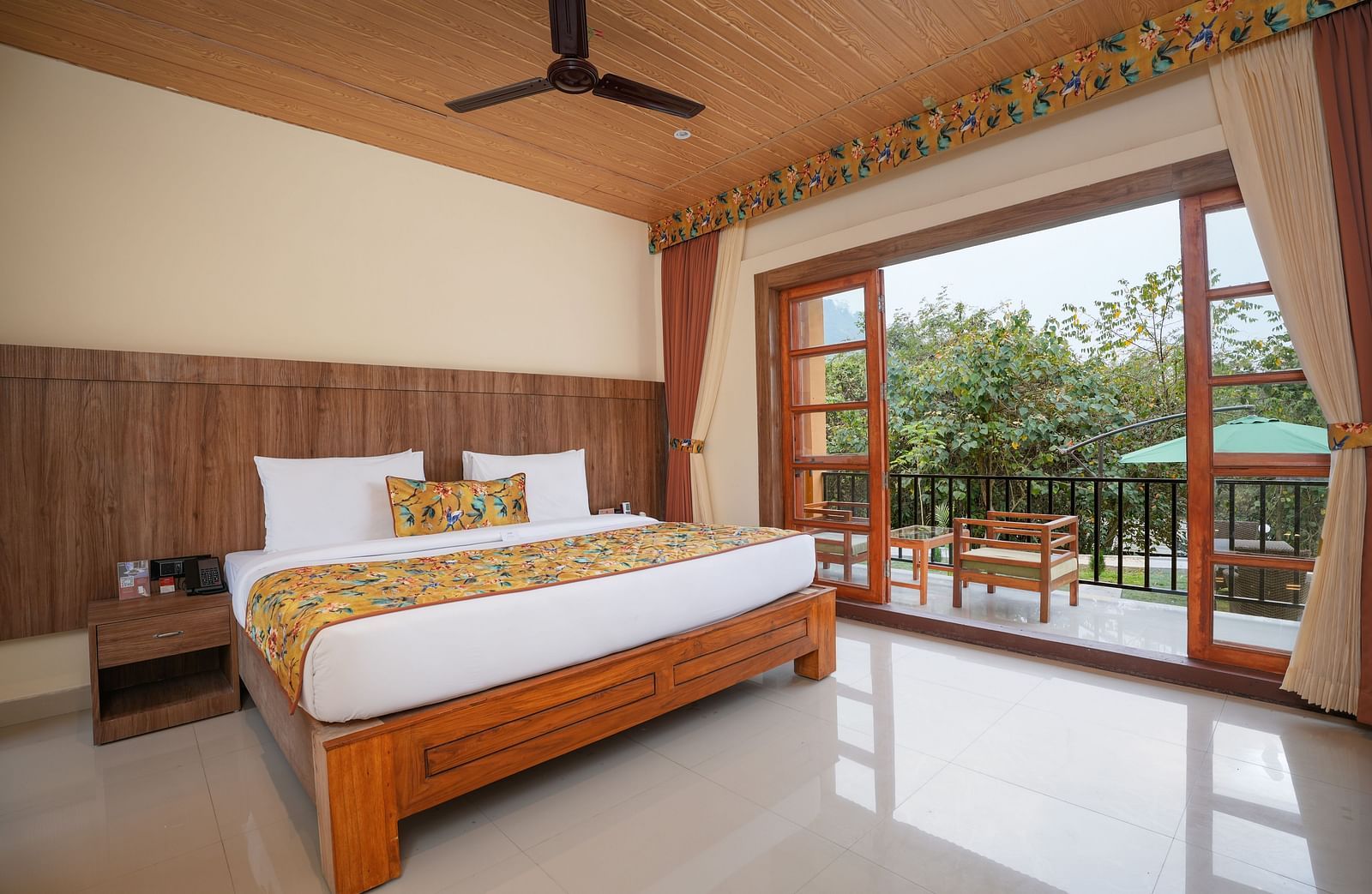 Bungalow featuring a spacious bed with wooden headboards, bedside table, and a large balcony at Summit Green Lake Tea Resort & Spa, Kaziranga