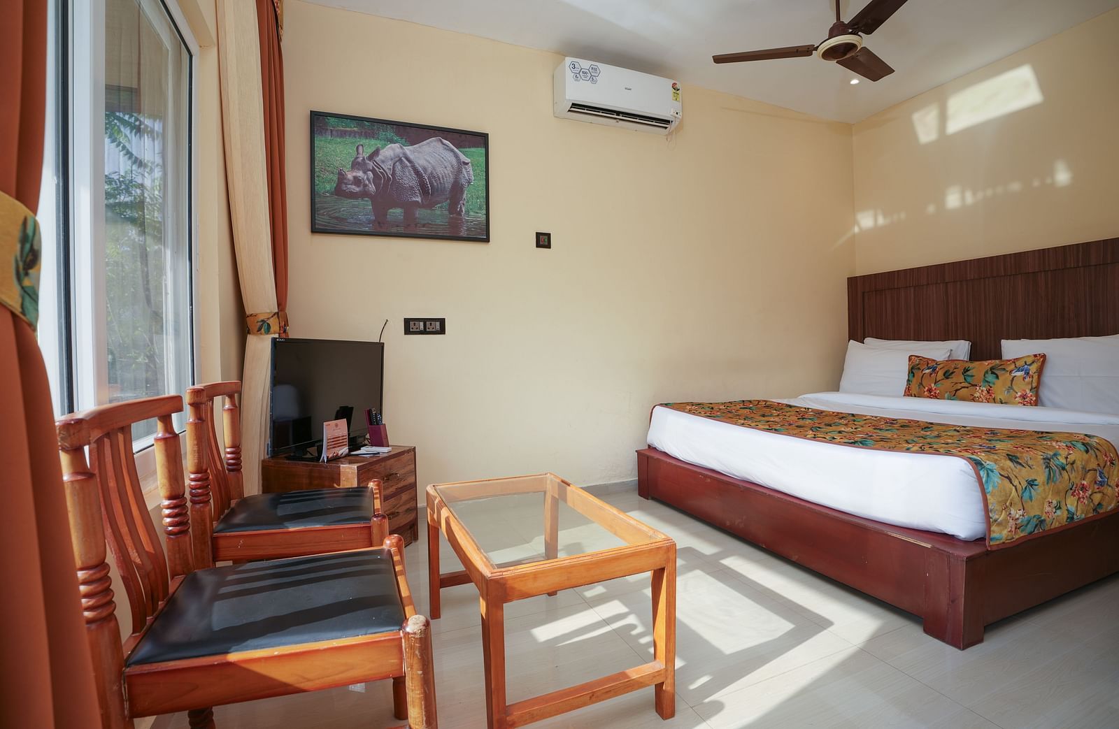 Deluxe Cottage featuring a spacious bed, television, air conditioner, glass table, and chairs at Summit Green Lake Tea Resort & Spa, Kaziranga