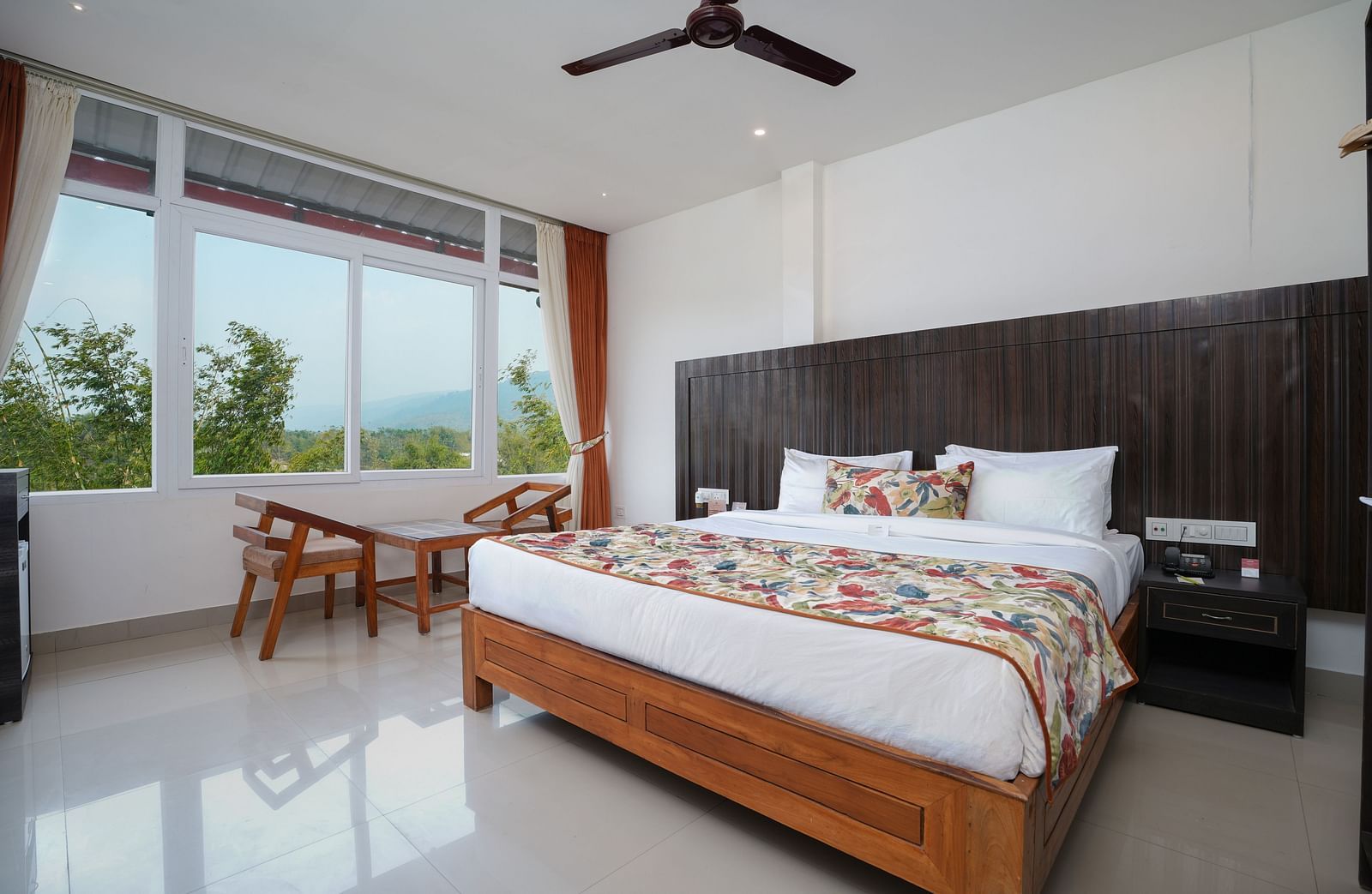 Deluxe room featuring large windows with a nature view, a spacious bed, air conditioning, wooden storage units, and a television at Summit Green Lake Tea Resort & Spa, Kaziranga4