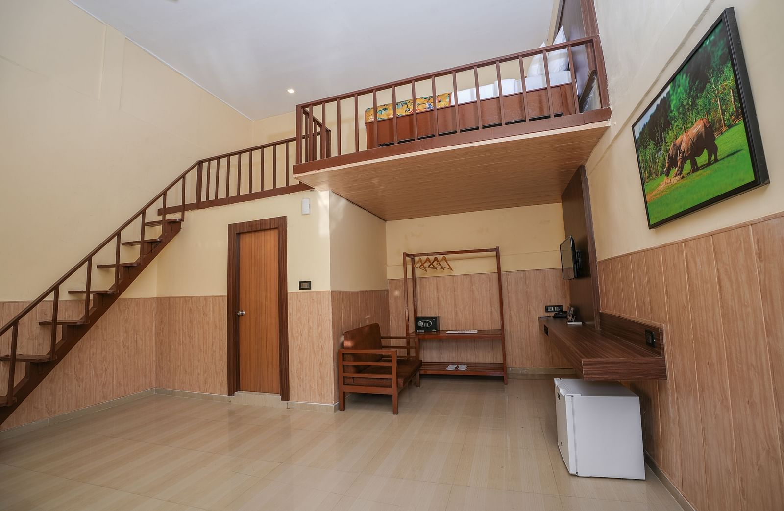Duplex room with balcony features a living area with wooden furniture, a wine fridge, wall-mounted television, and stairs leading to the spacious bedroom at Summit Green Lake Tea Resort & Spa, Kaziranga