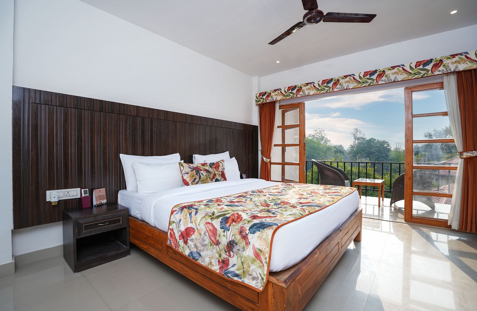 The suite with balcony offers a stunning nature view through large doors that open onto furniture and a glass table at Summit Green Lake Tea Resort & Spa, Kaziranga